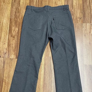 May include: A pair of dark grey straight-leg trousers with a back pocket and a small label on the back right pocket.