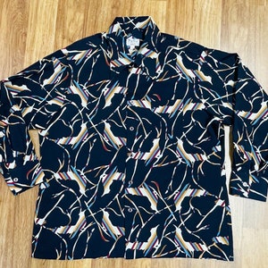 Puede incluir: Una camisa de manga larga con botones, fondo negro y estampado abstracto de colores. El estampado presenta líneas finas y formas en tonos de azul, rojo, blanco y beige.