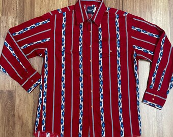 May include: A long-sleeved shirt with red, blue and white stripes and a geometric pattern. The shirt has a button-down collar and a single chest pocket.