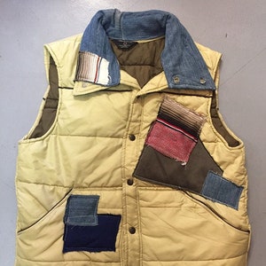 May include: A yellow quilted vest with a denim collar and multiple fabric patches in various colors and patterns.