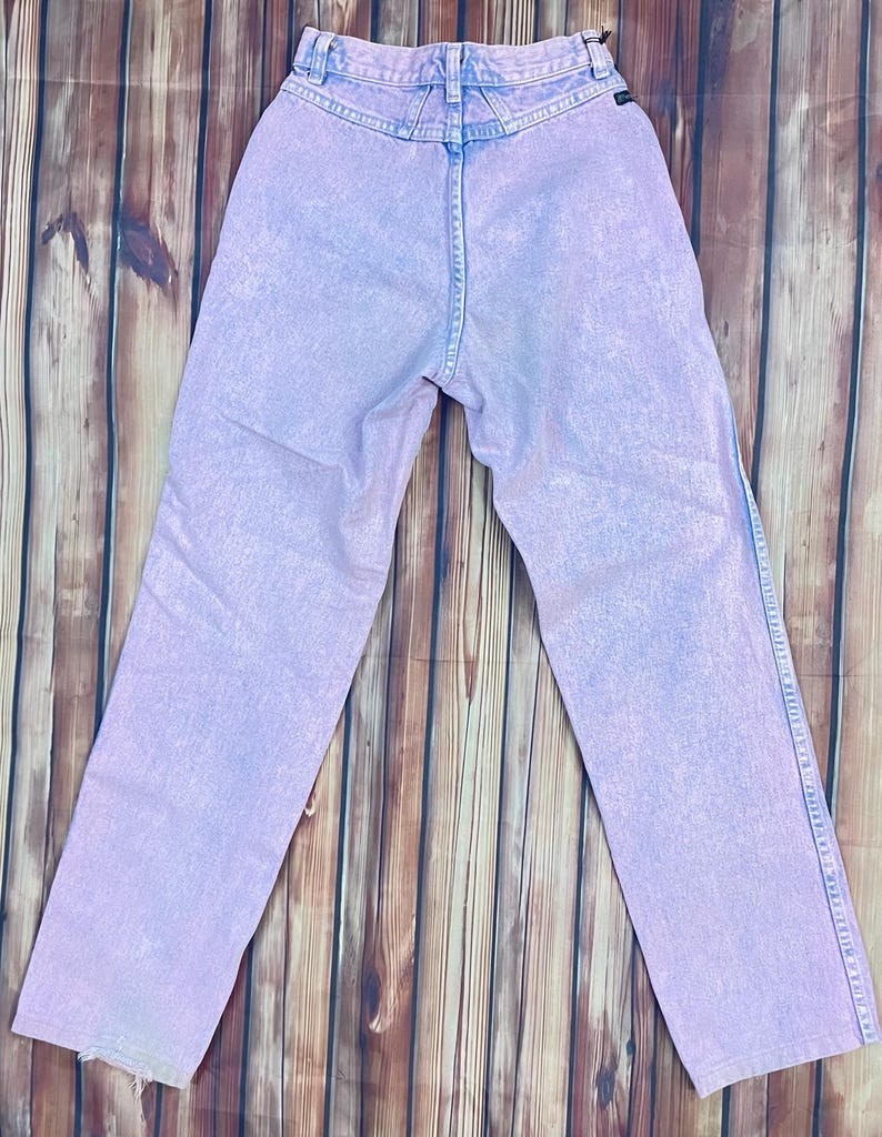 Pu&ograve; includere: Jeans in denim lilla chiaro con vita alta e classico design a cinque tasche. I jeans hanno un aspetto sbiadito, lavato con acidi e un taglio dritto. La vista posteriore mostra i passanti per la cintura e l'etichetta del marchio.