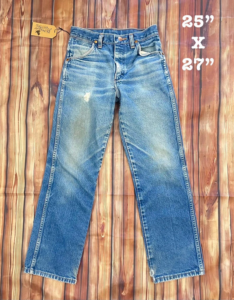 May include: Vintage blue denim jeans with a faded wash. The jeans are straight-legged and have a classic five-pocket design. The tag reads "The Packard Vintage". The jeans measure 25" x 27".