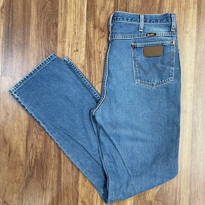 May include: A pair of light blue denim jeans with a brown leather patch on the back pocket that says "Wrangler".