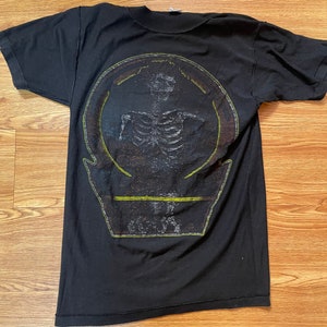 Puede incluir: Camiseta negra con un estampado gr&aacute;fico de un esqueleto en un c&iacute;rculo con el texto "O.S.T.R." debajo.