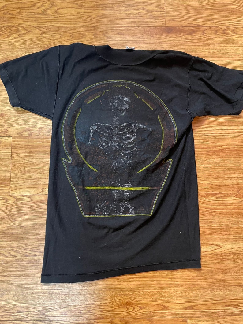 Puede incluir: Camiseta negra con un estampado gr&aacute;fico de un esqueleto en un c&iacute;rculo con el texto "O.S.T.R." debajo.