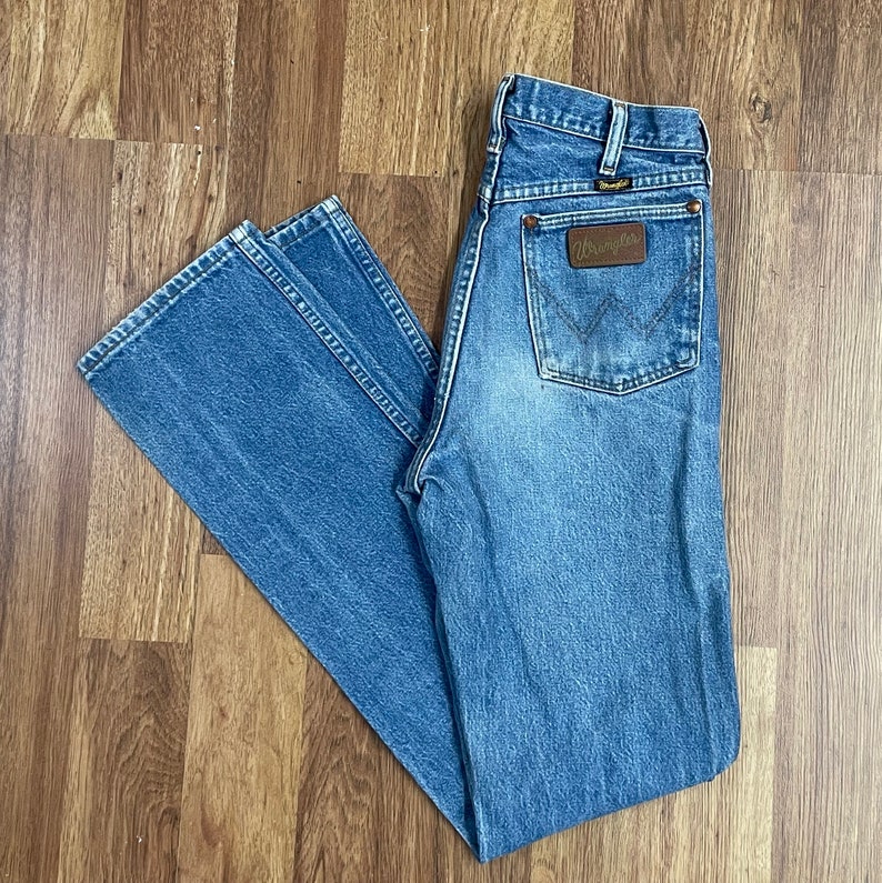 May include: A pair of blue denim jeans with a brown leather Wrangler patch on the back pocket.