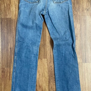 May include: A pair of blue denim jeans with a brown leather Wrangler label on the back pocket.