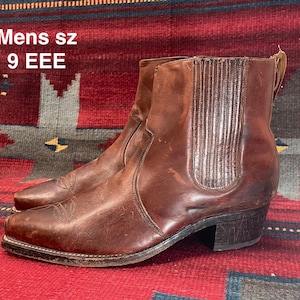 Może przedstawiać: Para brązowych skórzanych botków w stylu western. Buty mają spiczasty nosek, obcas i elastyczne panele boczne. Widoczny jest tekst "Mens sz 9 EEE".