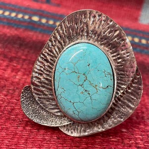May include: A silver ring with a large turquoise stone set in a textured, floral-shaped design.