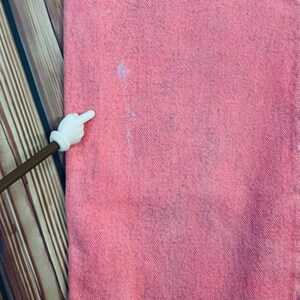 May include: Close-up of pink denim fabric with subtle blue and white markings. The fabric has a textured appearance, and the color is evenly distributed. The image is well-lit, highlighting the details of the material.