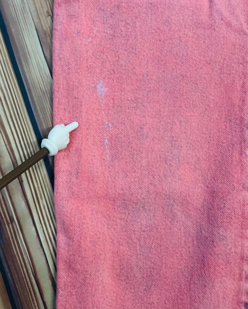 May include: Close-up of pink denim fabric with subtle blue and white markings. The fabric has a textured appearance, and the color is evenly distributed. The image is well-lit, highlighting the details of the material.