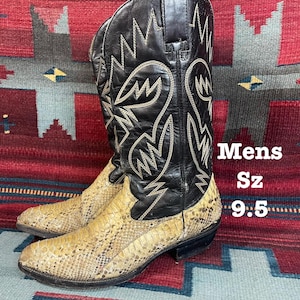 May include: Cowboy boots with a black leather upper and snakeskin-patterned foot. The boots feature decorative stitching and are labelled "Mens Sz 9.5". The boots are displayed on a patterned rug.