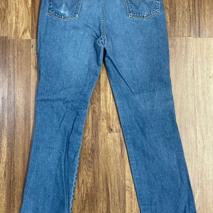 Może przedstawiać: Dżinsy z niebieskiego denimu z brązową sk&oacute;rzaną naszywką na tylnej kieszeni z napisem "Wrangler".