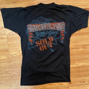 Puede incluir: Camiseta negra con un gr&aacute;fico de una rosa y el texto "Grateful Dead 1966-1980 Sold Out"