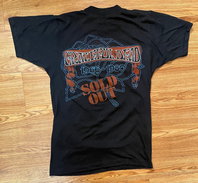 Puede incluir: Camiseta negra con un gr&aacute;fico de una rosa y el texto "Grateful Dead 1966-1980 Sold Out"