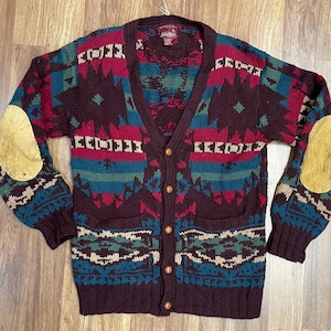 Könnte beinhalten: Eine bordeauxfarbene Strickjacke mit Knopfleiste und V-Ausschnitt, die ein geometrisches Muster in Türkis, Creme und Bordeaux zeigt. Der Pullover hat beige Ellbogenpatches und zwei Vordertaschen. Der Pullover ist aus Strickmaterial.