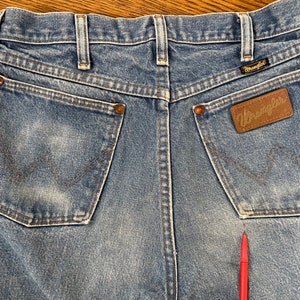 May include: A pair of blue denim jeans with a brown leather Wrangler label on the back pocket. The jeans have a faded look and are made of a soft, comfortable material.