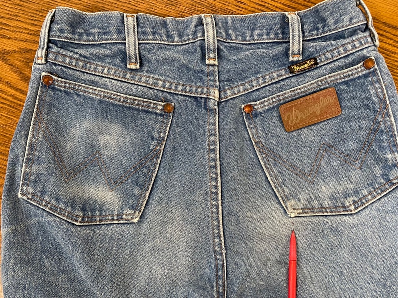 May include: A pair of blue denim jeans with a brown leather Wrangler label on the back pocket. The jeans have a faded look and are made of a soft, comfortable material.