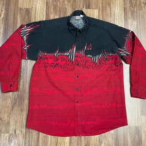 May include: A long-sleeved button-up shirt with a black and red abstract pattern. The shirt has a black collar and cuffs.