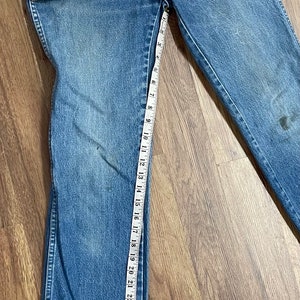 May include: A pair of blue denim jeans with a measuring tape along the inseam. The jeans are 33 inches long.
