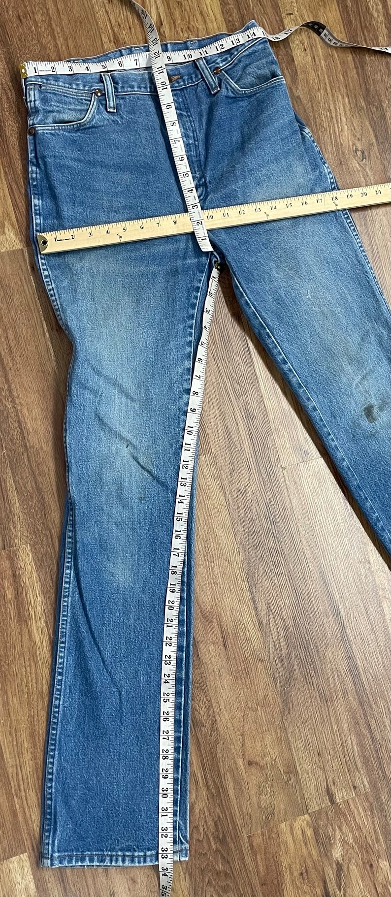 May include: A pair of blue denim jeans with a measuring tape along the inseam. The jeans are 33 inches long.
