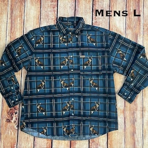 Puede incluir: Camisa de manga larga talla L, con un diseño de cuadros azules y ilustraciones de ciervos. Tiene cuello abotonado, bolsillo en el pecho y puños abotonados. El texto "MENS L" es visible.