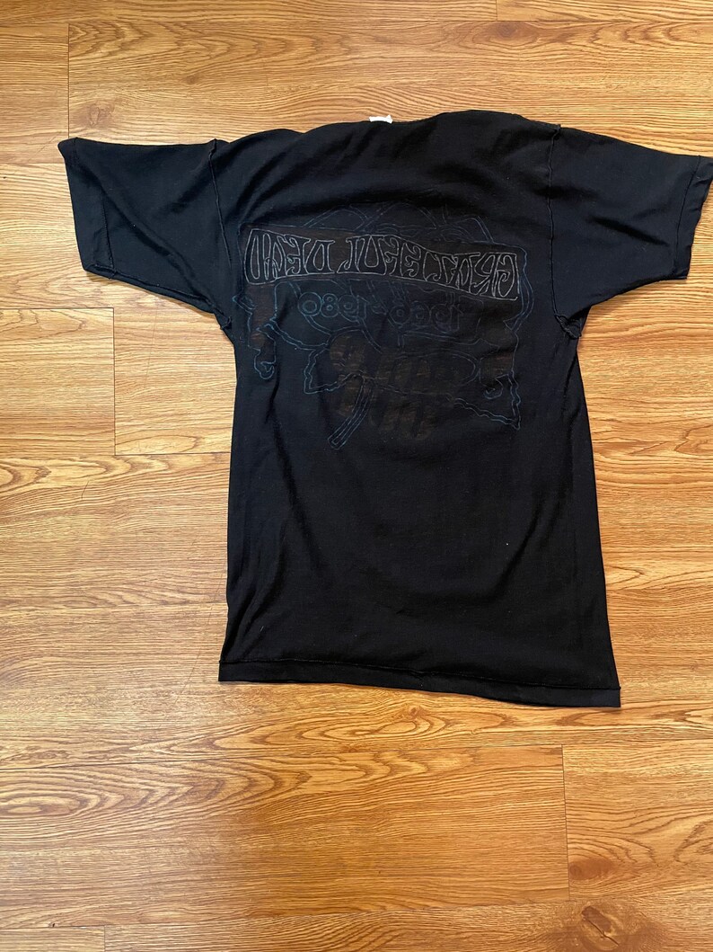 Puede incluir: Camiseta negra con un estampado gr&aacute;fico blanco de la banda "Grateful Dead" con el texto "1965-1995" y "The Grateful Dead" en la parte posterior.