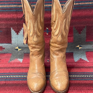 May include: A pair of tan leather cowboy boots with flame-like stitching. The boots are tall, with pointed tops and a worn appearance. The text "Ladies size 9" is visible at the bottom of the image.