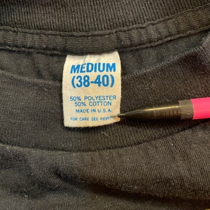 Puede incluir: Una etiqueta de ropa azul y blanca con el texto "MEDIUM (38-40)" y "50% POLI&Eacute;STER 50% ALGOD&Oacute;N HECHO EN EE. UU. PARA EL CUIDADO VER EL REVERSO"