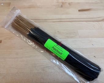 May include: A clear plastic bag containing a bundle of incense sticks. The sticks are dark brown with lighter brown tips. A green label reads "Patchouli" and "Exotic Incense Sticks". The bag is on a light wood surface.