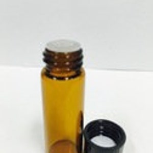 Op de afbeelding: Een klein amberkleurig glazen flesje met een zwarte plastic dop. De fles is leeg en heeft een witte plastic voering in de dop.