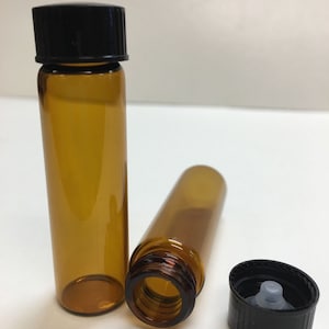 May include: Two amber glass bottles with black screw-on caps. One bottle is lying on its side, the other is standing upright. The cap of the bottle lying on its side is off and is lying next to the bottle.