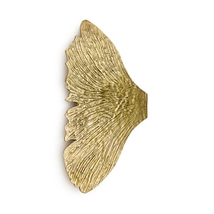 May include: A gold-coloured metal wall decor in the shape of a ginkgo leaf. The leaf has a textured surface and is a modern and stylish design.