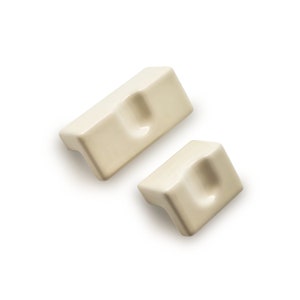 Puede incluir: Dos soportes de esquina para estantes de cerámica de color blanco roto con un borde redondeado y un área hundida en el centro.