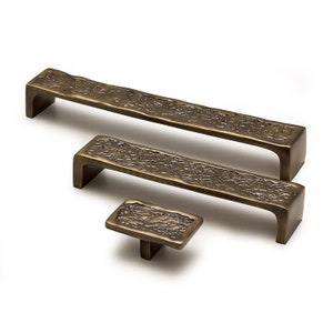 Può includere: Set di tre elementi hardware per mobili color bronzo. Il set include due maniglie rettangolari e un pomello quadrato. Ogni pezzo ha una superficie strutturata, che conferisce loro un aspetto rustico. L'hardware è progettato per mobili e armadi.