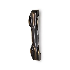 May include: A bronze-colored, elongated door pull with a curved, organic design. The hardware has a smooth, polished finish with subtle highlights and shadows, suggesting a metallic material. The door pull is mounted vertically against a white background.