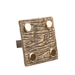 May include: A square-shaped, textured, bronze-colored door handle with four gold-colored accents.