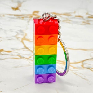 May include: A rainbow-coloured LEGO keychain with a silver key ring. The keychain is made up of six stacked LEGO bricks, each a different colour of the rainbow.