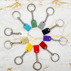 Pu&ograve; includere: Una collezione di portachiavi colorati con ciondoli a forma di mattoncino in vari colori, tra cui blu, verde, grigio, nero, viola, rosso e giallo. Ogni portachiavi ha un anello e una catena color argento.