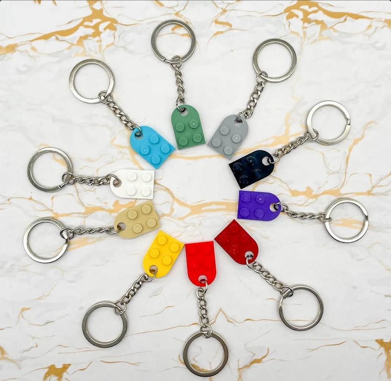 Pu&ograve; includere: Una collezione di portachiavi colorati con ciondoli a forma di mattoncino in vari colori, tra cui blu, verde, grigio, nero, viola, rosso e giallo. Ogni portachiavi ha un anello e una catena color argento.