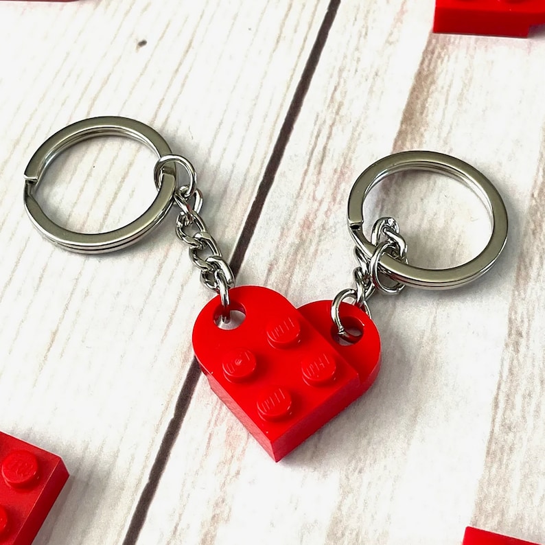 Pu&ograve; includere: Un paio di portachiavi rossi a forma di cuore realizzati con mattoncini ad incastro. Ogni portachiavi ha un anello e una catena in metallo argentato. Un'idea regalo divertente.