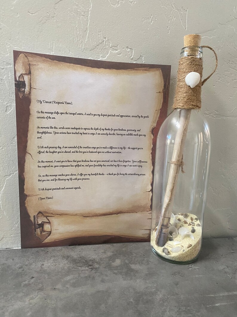 May include: A clear glass bottle with a cork stopper, twine, and a seashell decoration. Inside the bottle are sand, seashells, and a rolled-up scroll. A printed scroll with text is next to the bottle.