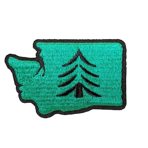 Op de afbeelding: Geborduurde patch met de omtrek van de staat Washington in groen, met een zwarte rand. Een zwarte boomafbeelding staat in het midden van de groene vorm. De patch is bedoeld voor kleding of accessoires.