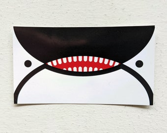 May include: A white sticker with a black and red whale illustration. The whale has a large, open mouth with red teeth and a black outline. The whale's eyes are black circles.