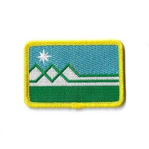 May include: An embroidered patch with a yellow border, featuring a blue sky, white mountains, and a white star. The mountains are green and white, and the sky is a light blue.
