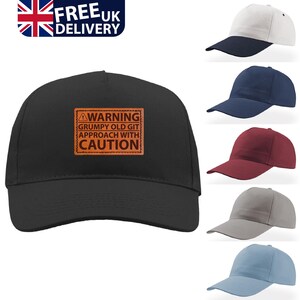 May include: A black baseball cap featuring a rectangular orange patch on the front with the text WARNING GRUMPY OLD GIT APPROACH WITH CAUTION. The image also displays five additional baseball caps in white, navy, maroon, grey, and light blue colours.