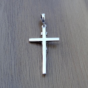 Puede incluir: Pendiente de plata en forma de cruz con un dise&ntilde;o detallado. La cruz est&aacute; sobre un fondo de madera.