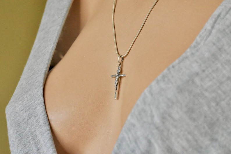 Puede incluir: Un collar de cadena de plata con un colgante de crucifijo de plata.