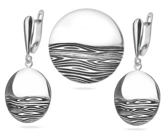 May include: A set of silver earrings and a pendant featuring a wavy, abstract design. The jewelry is made of polished silver and has a modern, minimalist style.