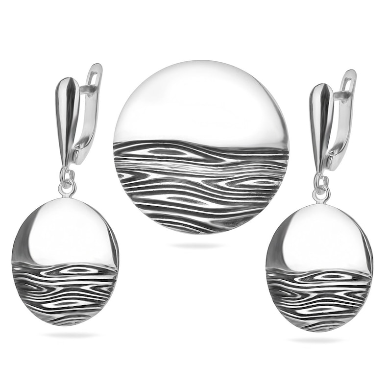 Puede incluir: Un conjunto de pendientes y un colgante de plata con un dise&ntilde;o ondulado abstracto. Las joyas est&aacute;n hechas de plata pulida y tienen un estilo moderno y minimalista.